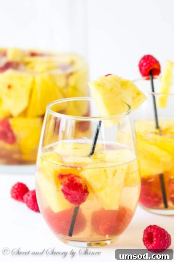 Vibrant Pineapple Raspberry Sangria in a glass pitcher with fresh pineapple and raspberries