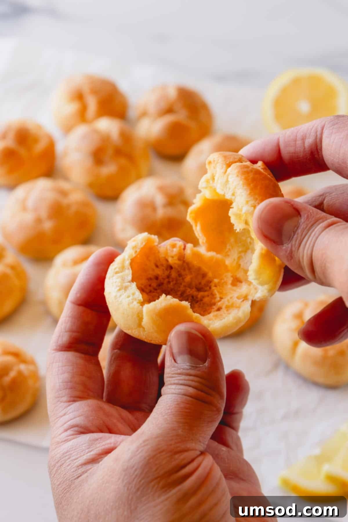 Zesty Lemon Cloud Puffs 11 A cream puff shell being pulled apart, exposing its perfectly hollow, airy center, ready for filling.