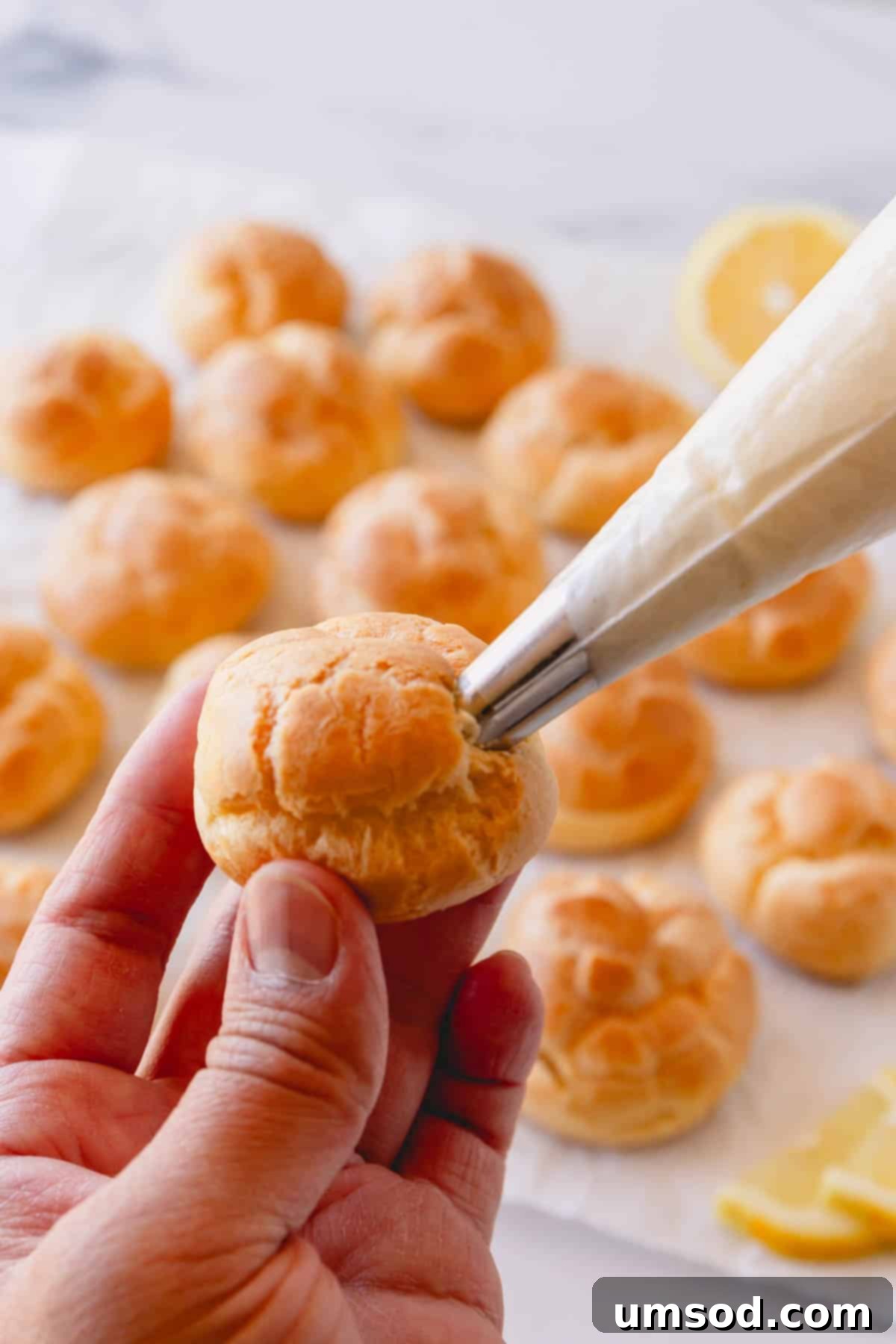 Zesty Lemon Cloud Puffs 13 A creme puff being filled with creamy lemon curd using a piping bag.