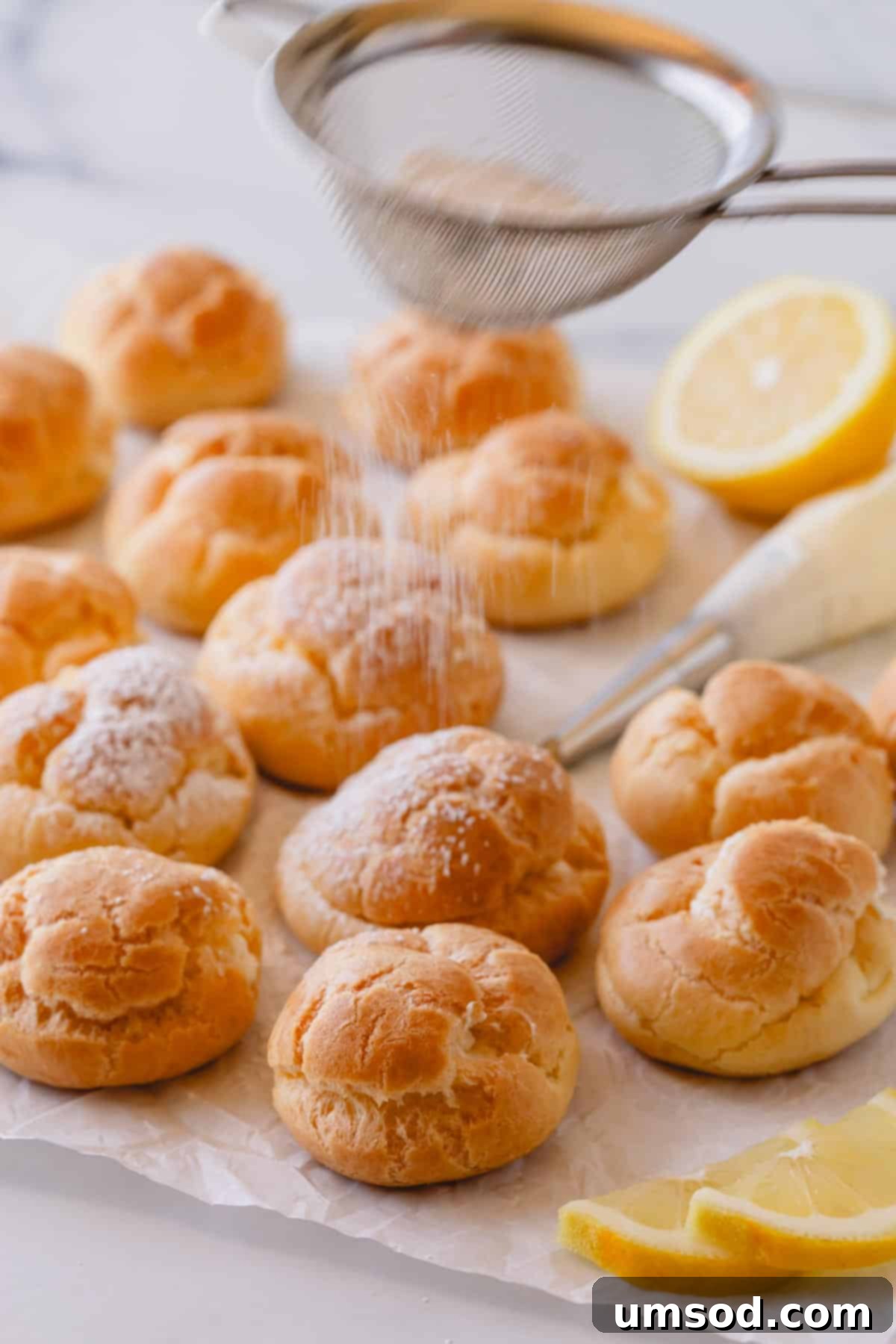 Zesty Lemon Cloud Puffs 14 Lemon creme puffs being dusted with a fine layer of powdered sugar for presentation.