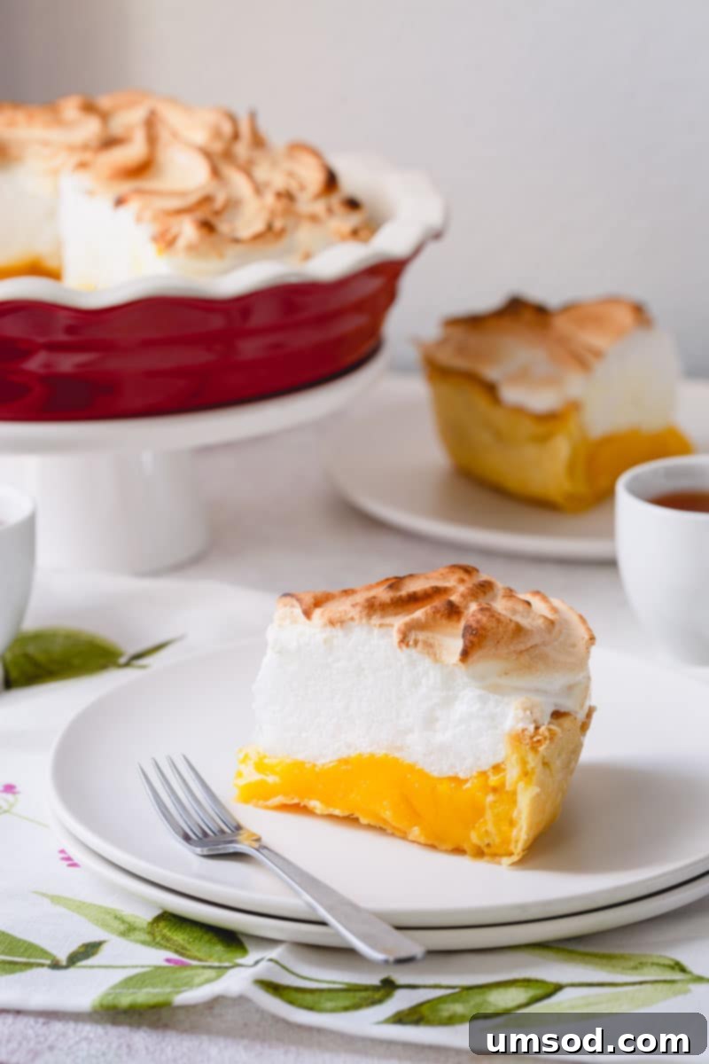 Zesty Lemon Cloud Pie 2 Two slices of lemon meringue pie on plates with the rest of the pie in the background, showcasing its golden meringue and vibrant filling.