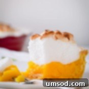 Zesty Lemon Cloud Pie 13 A slice of classic lemon meringue pie on a plate with a fork holding a bite.