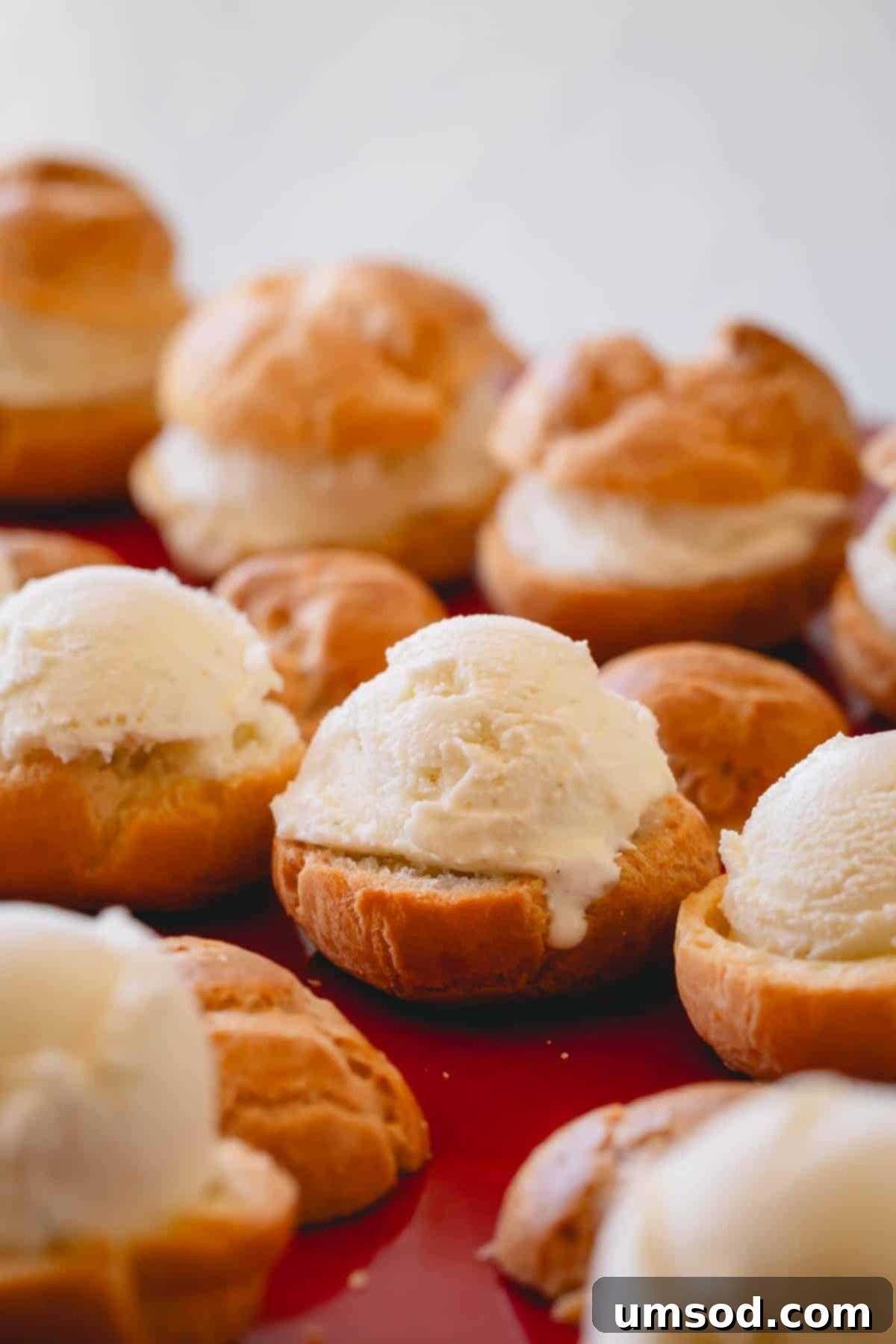 Vanilla ice cream being scooped into the hollow of a sliced profiterole shell.
