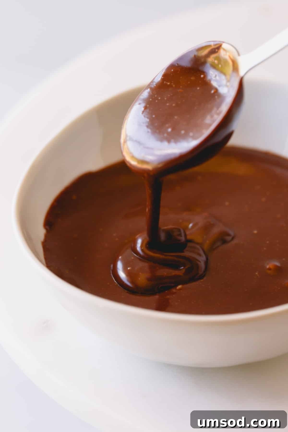 Smooth, rich chocolate ganache in a bowl, with a spoon lifting some, showcasing its perfect consistency.