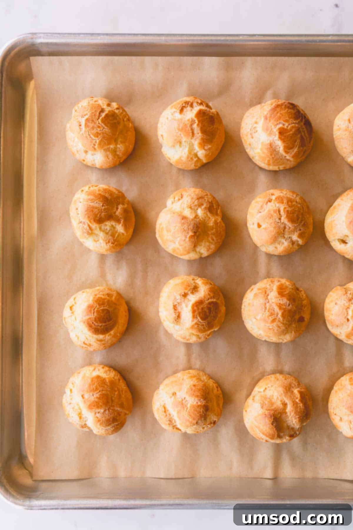 Perfectly baked, golden-brown profiterole shells resting on a baking sheet, fresh from the oven.