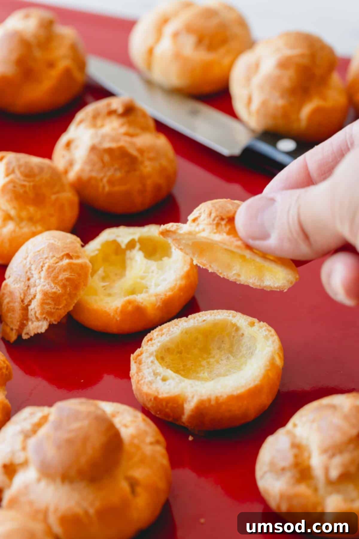 A profiterole shell being sliced open with a paring knife, revealing its hollow interior.