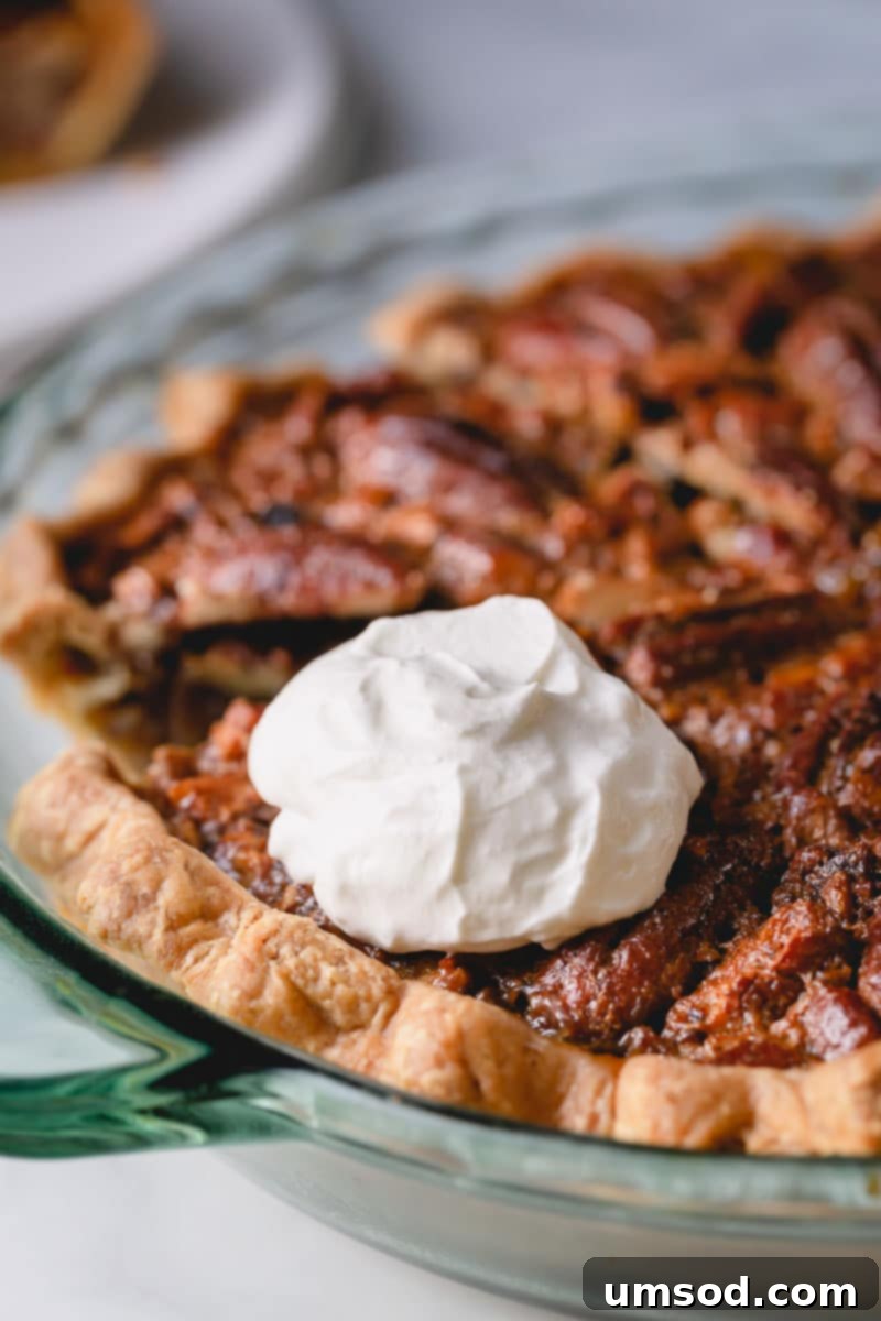 A delicious slice of pecan pie topped with a generous dollop of homemade yogurt whipped cream, ready to be enjoyed.