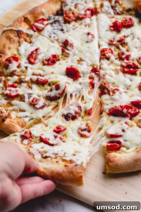 Slow-Roasted Tomato and Melted Cheese Pizza 2 Sliced pesto pizza with a delightful cheese pull, showcasing melted mozzarella and vibrant cherry tomatoes.