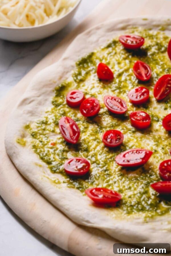 Slow-Roasted Tomato and Melted Cheese Pizza 3 Unbaked pizza generously topped with vibrant green pesto and perfectly sliced cherry tomatoes, ready for the oven.