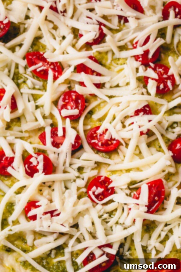 Slow-Roasted Tomato and Melted Cheese Pizza 4 An up-close shot of an unbaked pizza, highlighting the fresh pesto, cherry tomato halves, and shredded mozzarella before baking.