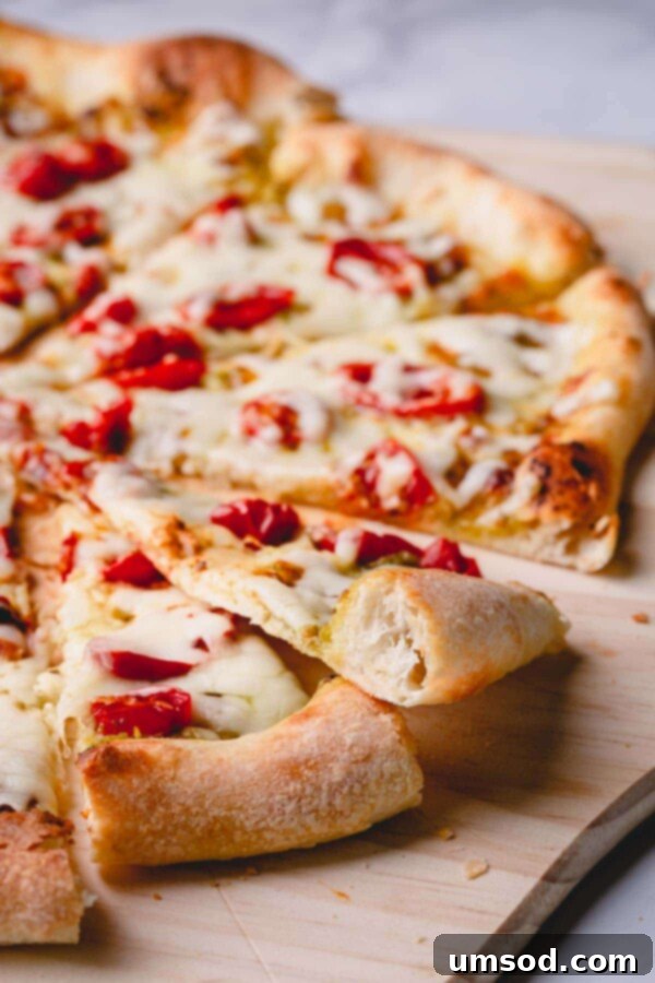 Slow-Roasted Tomato and Melted Cheese Pizza 8 A close-up of a perfectly baked and sliced pesto pizza, revealing an airy, crispy crust and melted toppings.