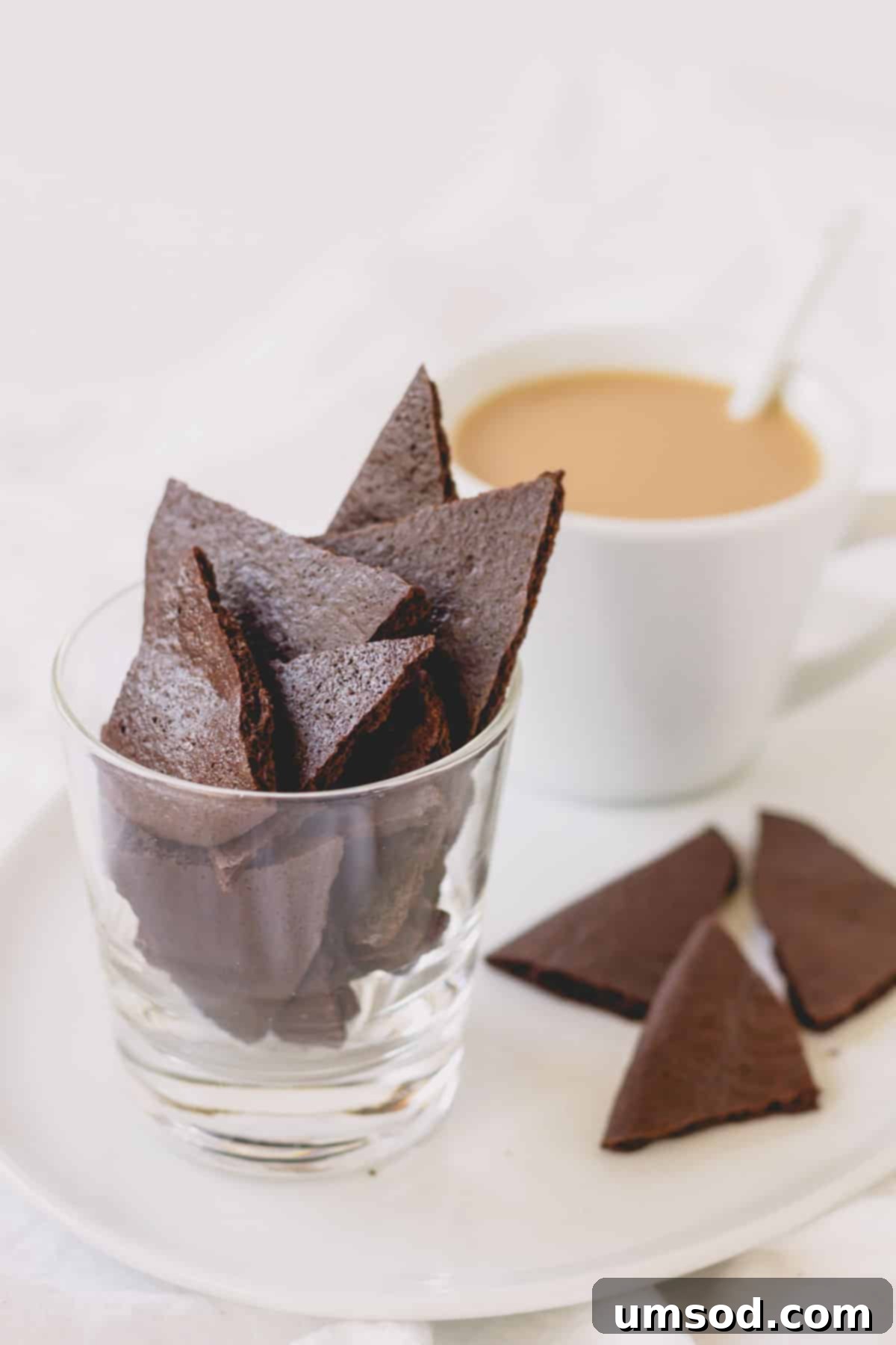 A charming platter featuring a cappuccino, a glass overflowing with brownie crisps, and a few scattered crisps on the tray.