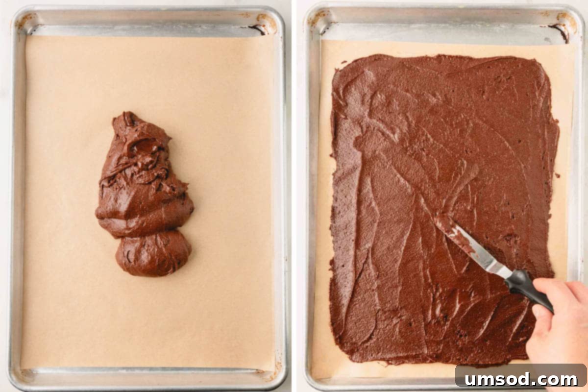 Brownie crisp batter being meticulously spread into a thin, even layer over a parchment-lined baking sheet using an offset spatula.