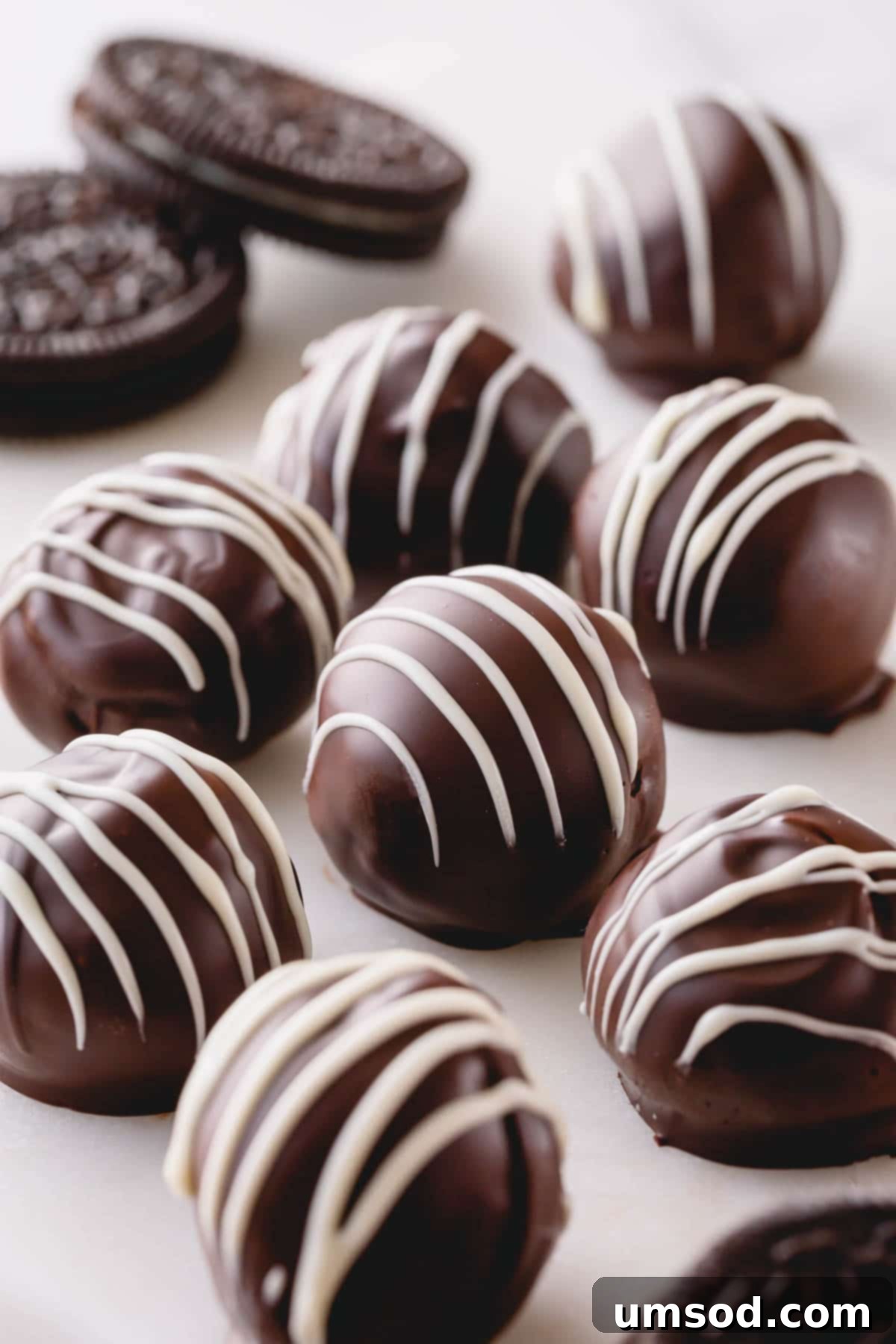 Dark chocolate Oreo balls with elegant white chocolate drizzle, presented beautifully on a platter.