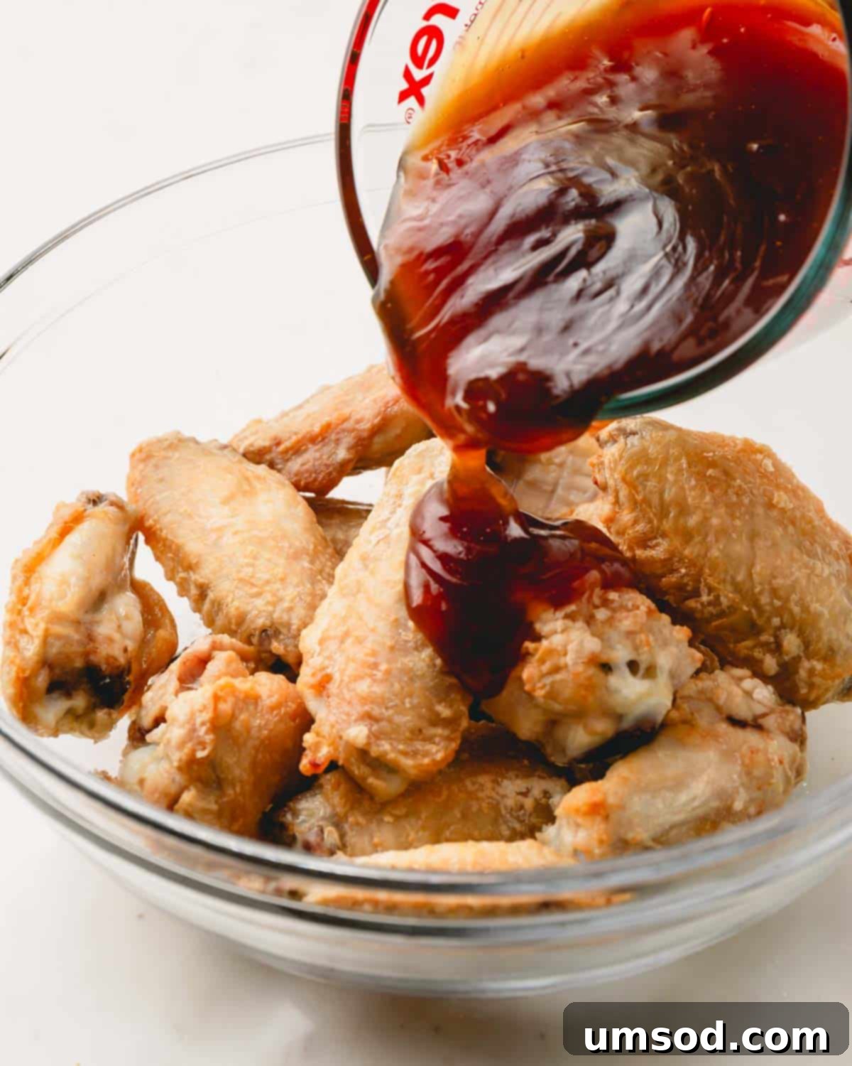 Sticky Teriyaki Chicken Wings 11 Homemade teriyaki sauce being poured generously over a bowl of freshly baked chicken wings, ensuring they are fully coated.
