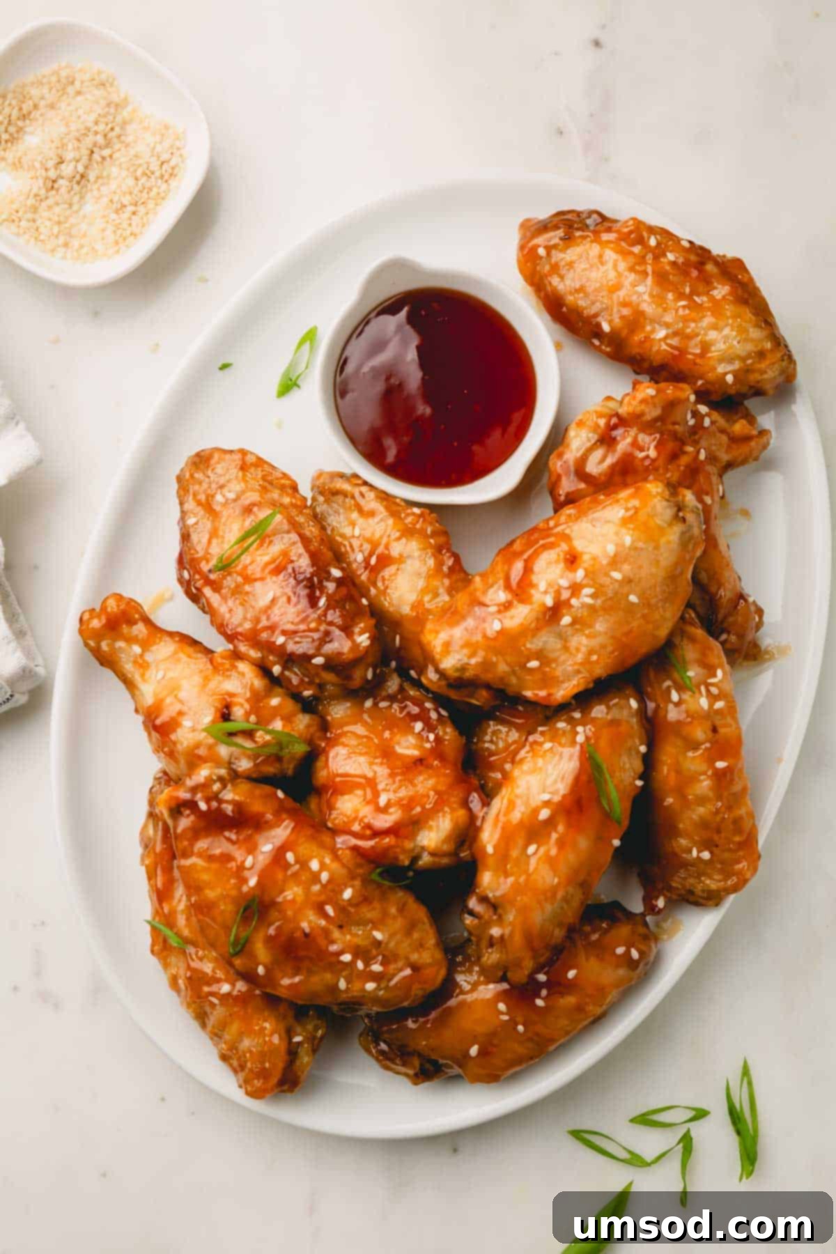 Sticky Teriyaki Chicken Wings 3 A platter brimming with golden, crispy honey teriyaki chicken wings, with a small bowl of extra teriyaki sauce on the side for dipping.