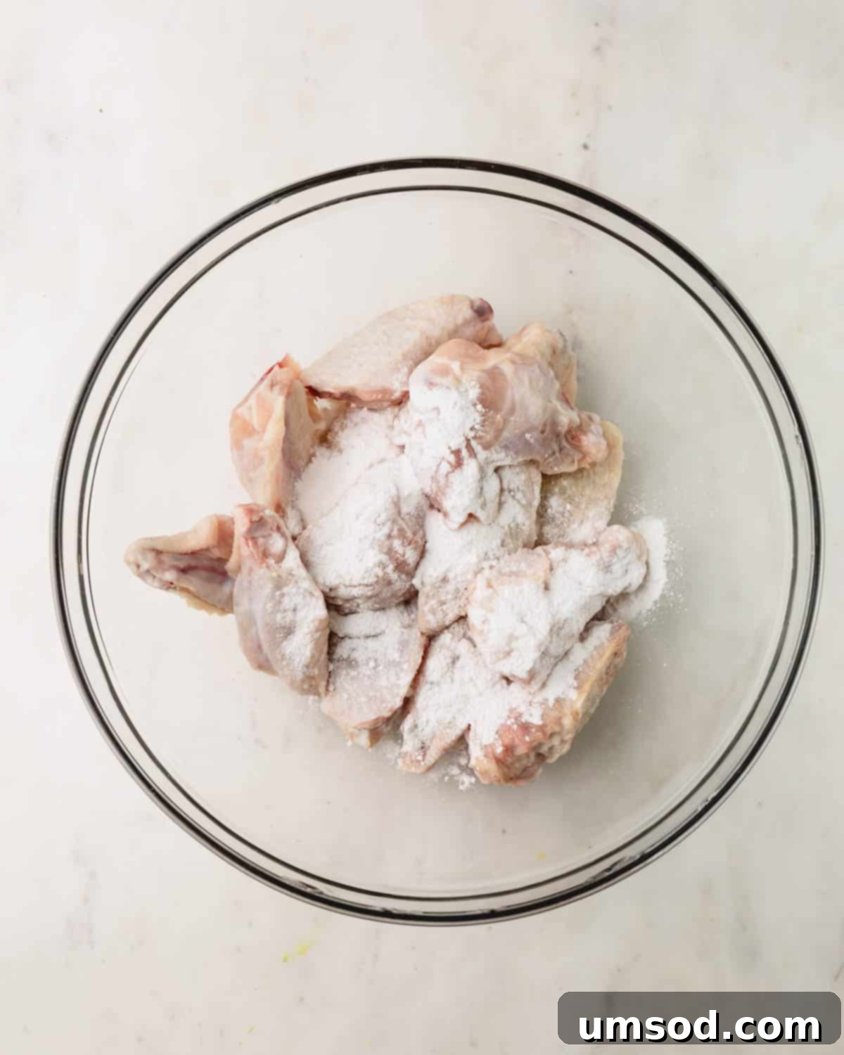 Sticky Teriyaki Chicken Wings 7 Raw chicken wings being tossed in a bowl with baking powder and salt, showing the coating process for crispy skin.