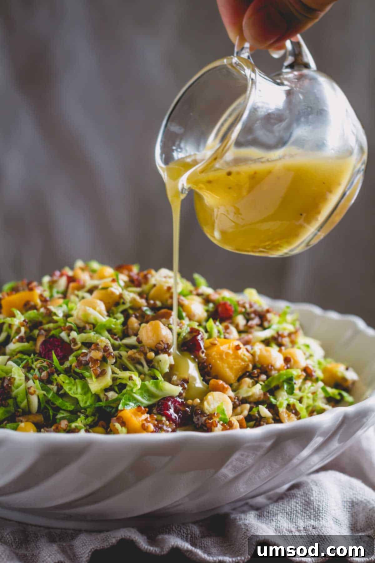 Roasted Brussels Sprout and Warm Quinoa Power Bowl 3 Homemade Honey Dijon dressing being drizzled over the warm quinoa Brussels sprouts salad in a serving bowl.