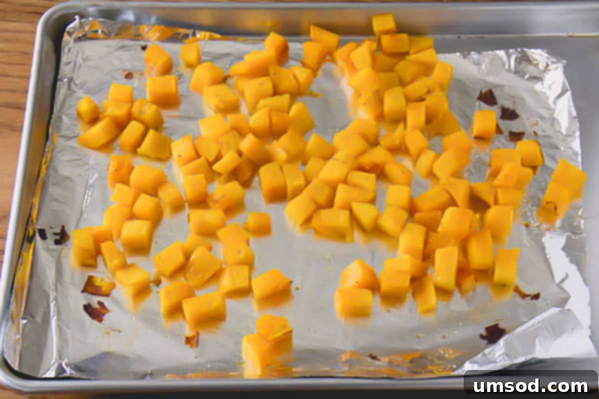 Roasted Brussels Sprout and Warm Quinoa Power Bowl 4 Cubed acorn squash tossed with olive oil, salt, and pepper arranged on a baking sheet lined with foil, ready for roasting.