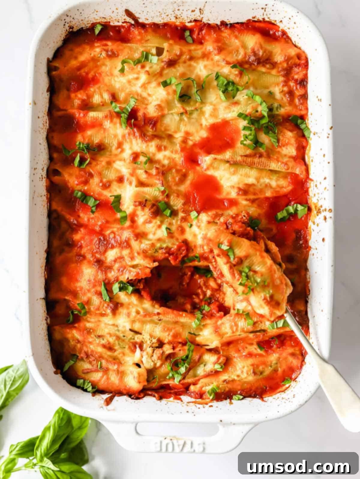 A dish of creamy pesto ricotta stuffed pasta shells with a serving spoon lifting one shell, garnished with fresh basil.