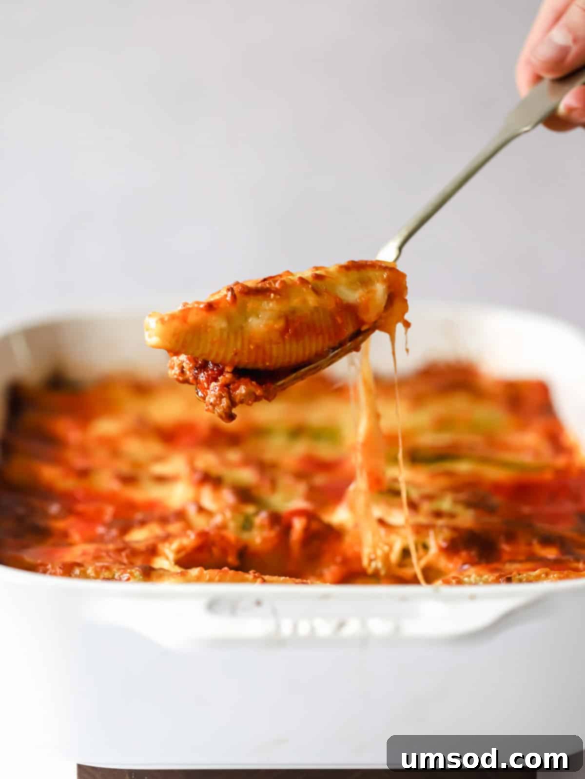 A serving spoon gracefully lifting a single pesto ricotta stuffed pasta shell from a hot, bubbling baking dish, showcasing the creamy filling and melted cheese.