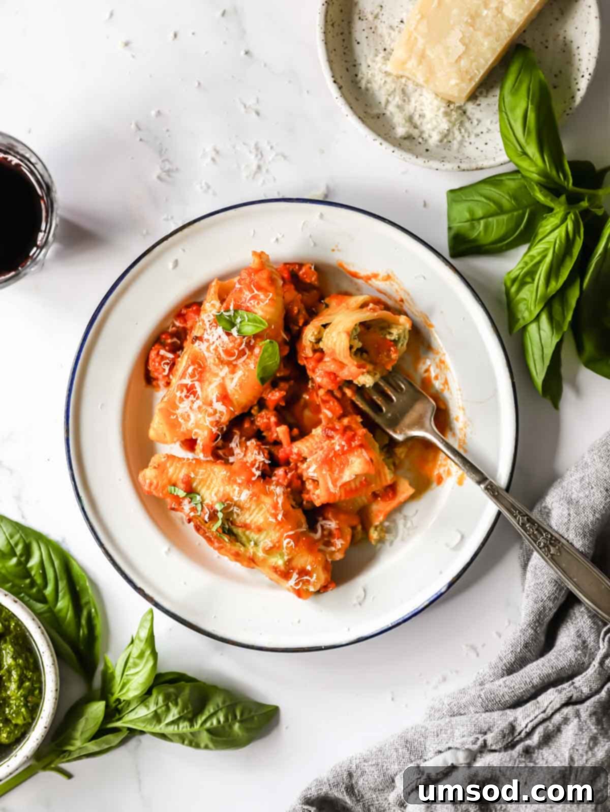 A plate generously filled with pesto ricotta stuffed pasta shells, garnished with fresh basil, with a fork holding one shell aloft.