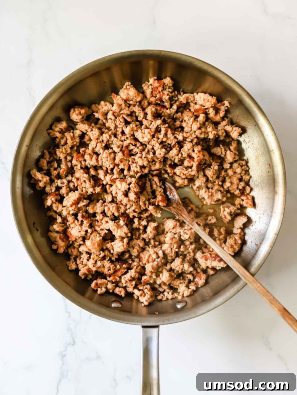 Browned Italian sausage sizzling in a skillet, ready to be drained.