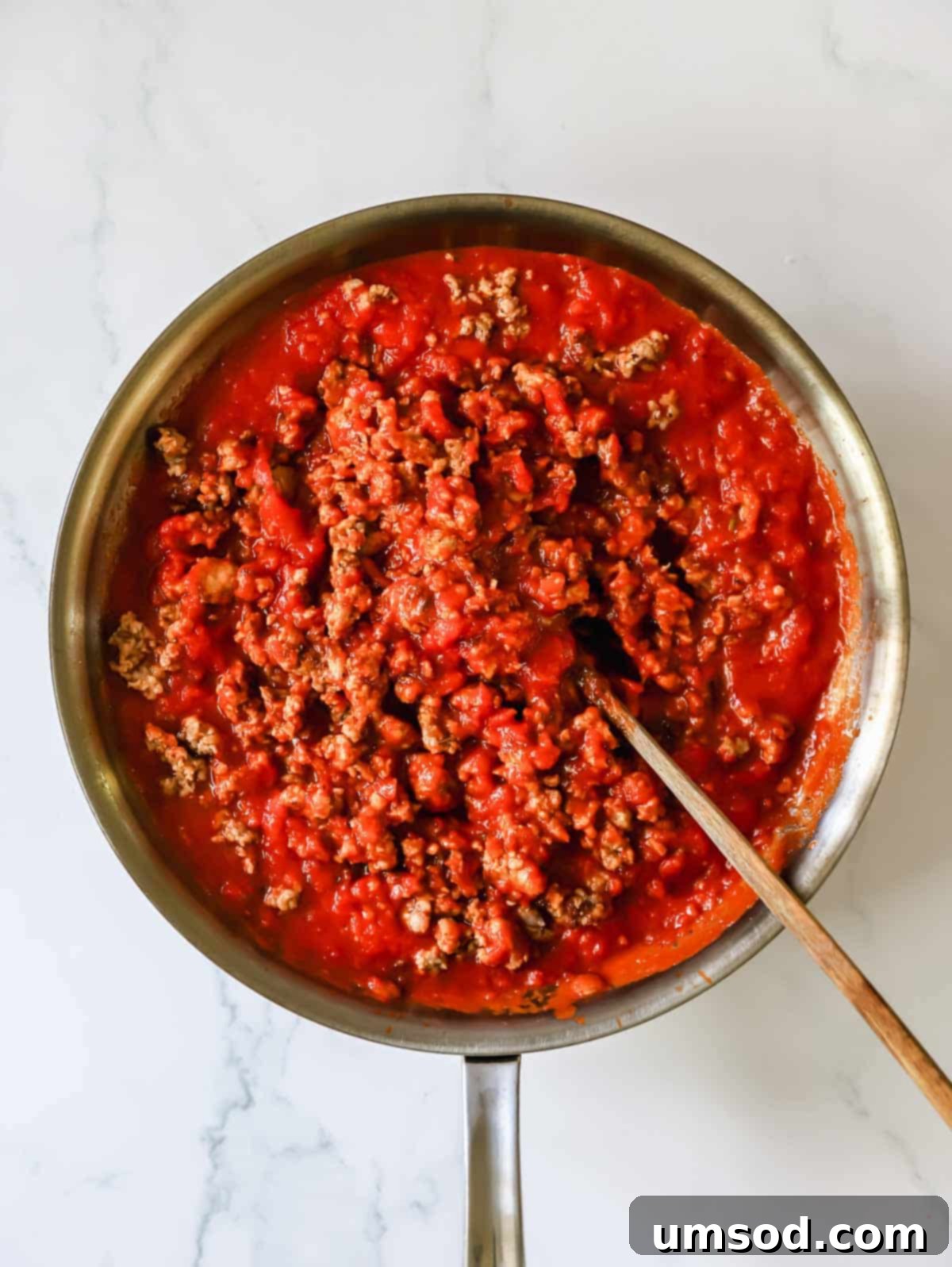 A rich pasta sauce simmering with browned Italian sausage in a skillet.