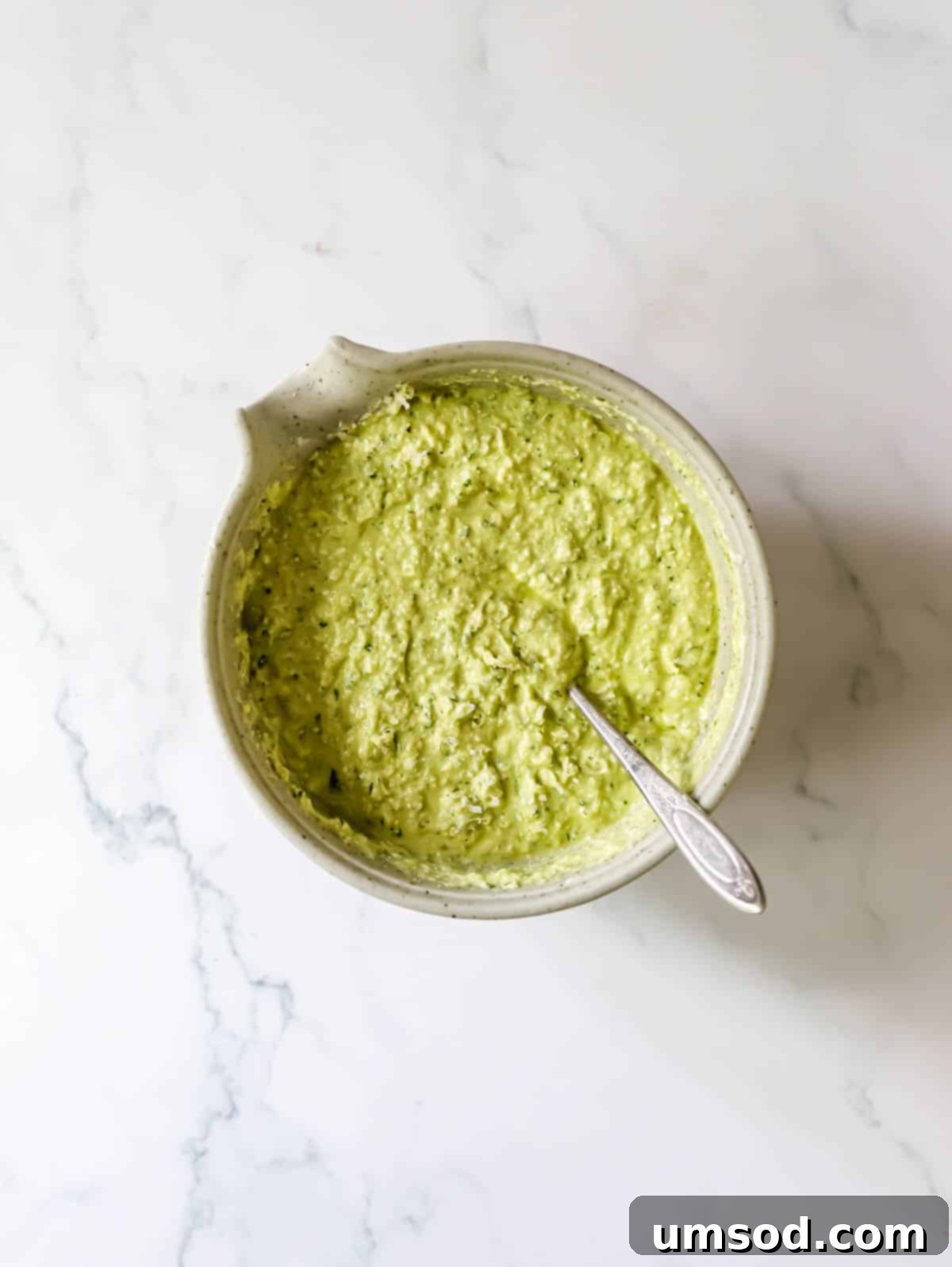 A jar of vibrant green pesto sauce with a spoon dipped in, highlighting its rich texture.