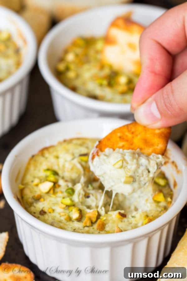 Five Ingredient Pesto Artichoke Dip 4 Close-up of bubbling Pesto Artichoke Dip in a small ramekin, garnished with pistachios.