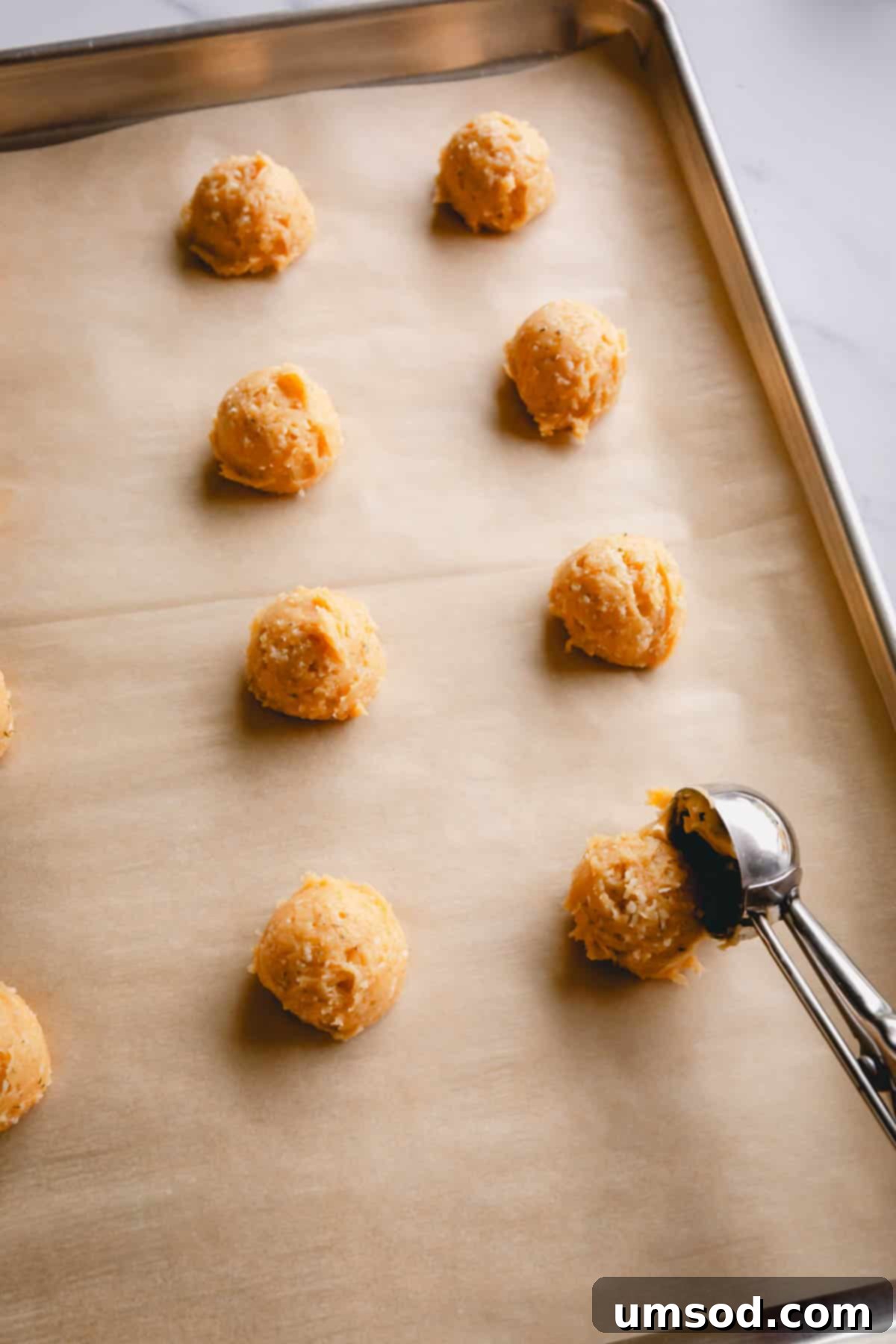 Havarti Cheese Gougères 9 Scooping cheese puffs dough with a cookie dough scoop onto a baking sheet lined with parchment paper, showing proper spacing.