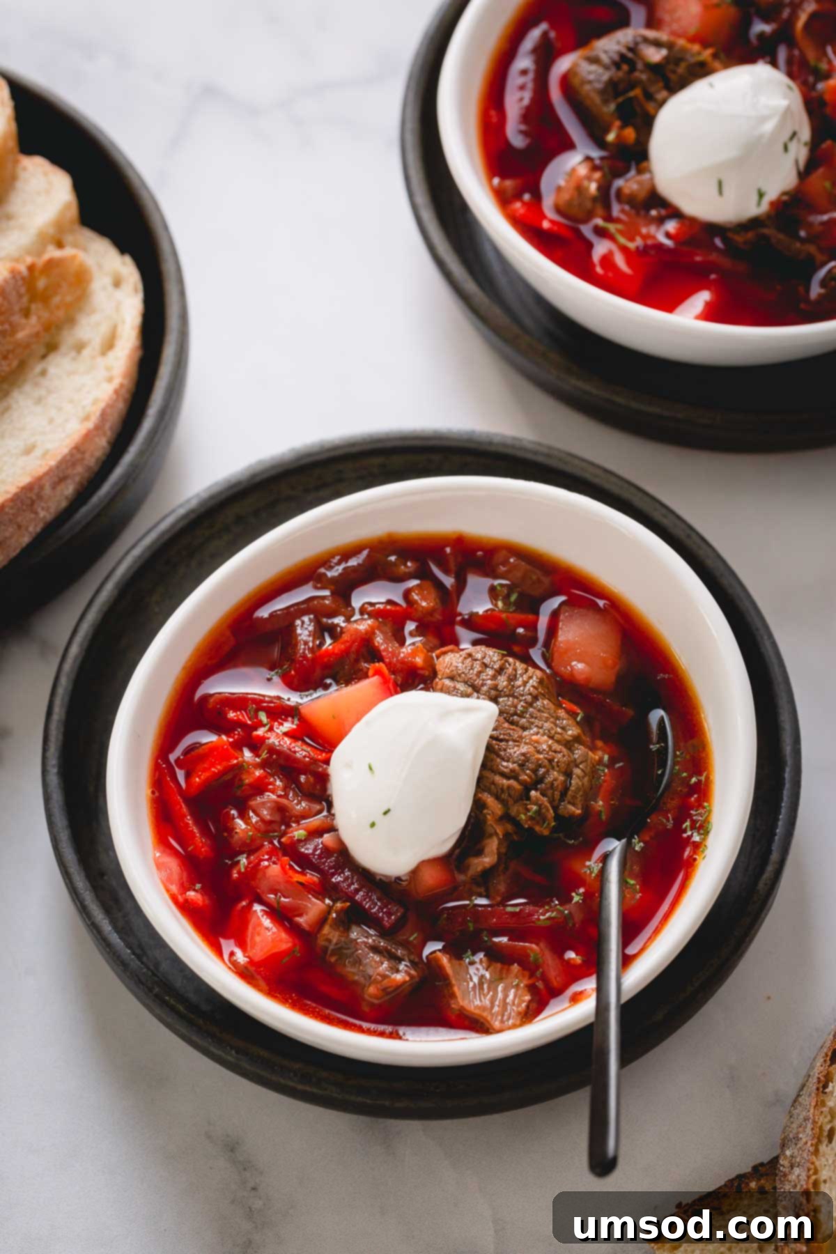 Beef borscht soup in a white bowl topped with dollop of sour cream.