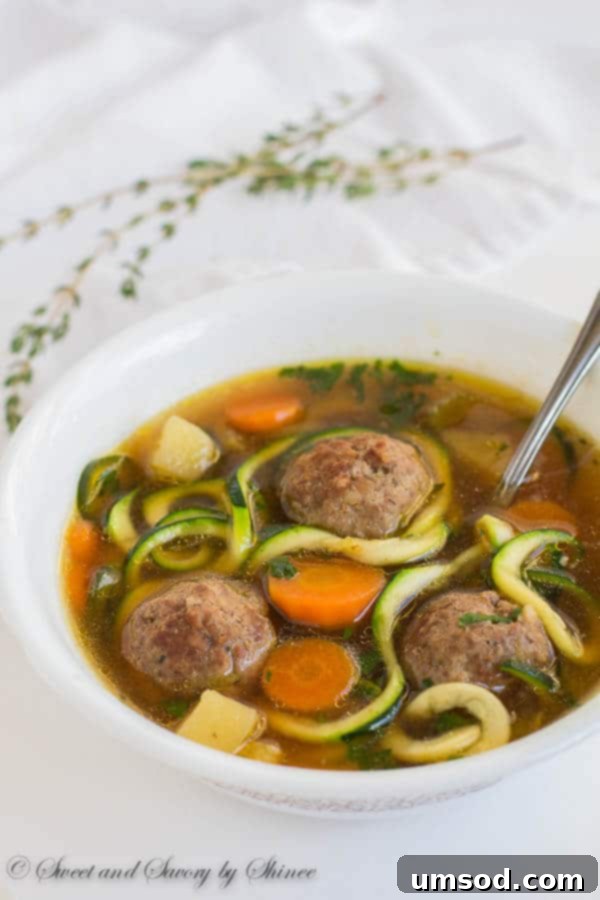 A close-up shot of vegetable meatball soup, showcasing tender, browned meatballs and perfectly cooked zucchini noodles amidst colorful vegetables.