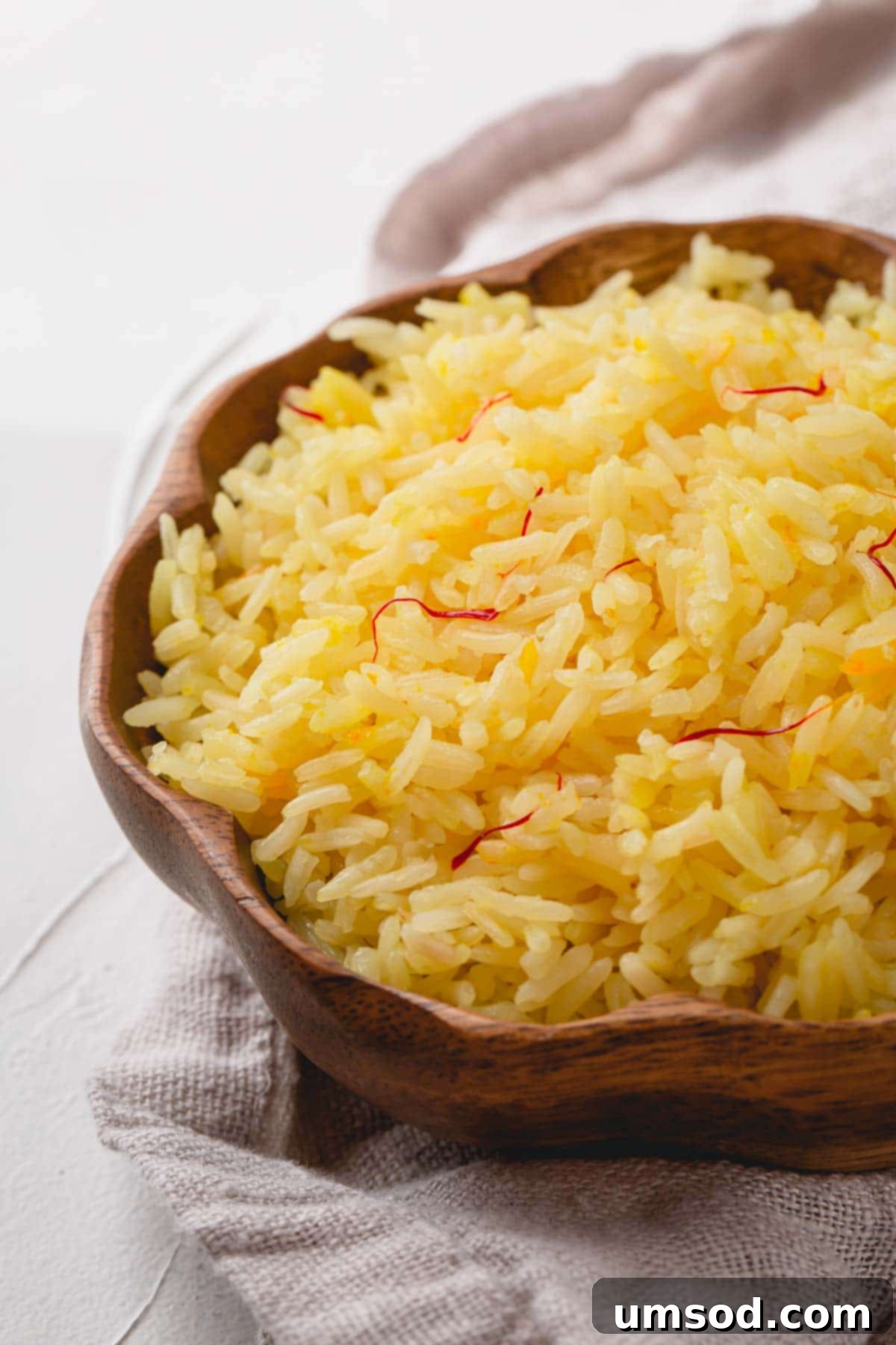 Fragrant Golden Pilaf 3 Close-up of perfectly cooked saffron rice in a rustic wooden bowl, showcasing its golden color and fluffy texture.