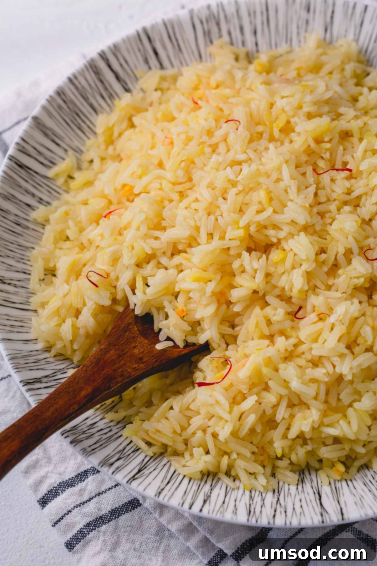 Fragrant Golden Pilaf 9 Saffron rice served in a white bowl with a wooden spoon, garnished with fresh herbs, ready for a meal.