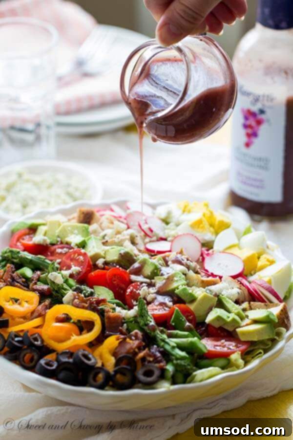 An overhead shot of a beautifully arranged Spring Cobb Salad, highlighting crisp greens, colorful vegetables, and rich proteins, drizzled with Marzetti® dressing.