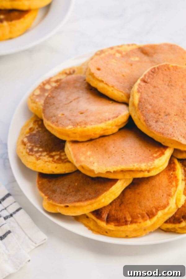 Pillowy Pumpkin Pancakes 3 A large serving platter piled high with golden brown pumpkin pancakes, glistening slightly, ready to be enjoyed.