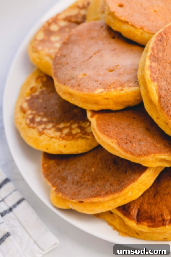 Pillowy Pumpkin Pancakes 5 A vibrant, warm shot of a large pile of pumpkin pancakes on a serving platter, invitingly ready.