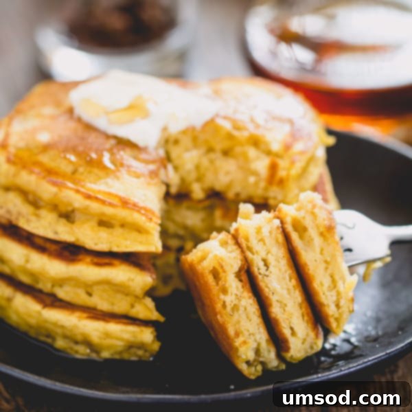 Pillowy Pumpkin Pancakes 6 A fork holding a piece of a pumpkin pancake, showing its fluffy interior, with a stack of pancakes blurred in the background.