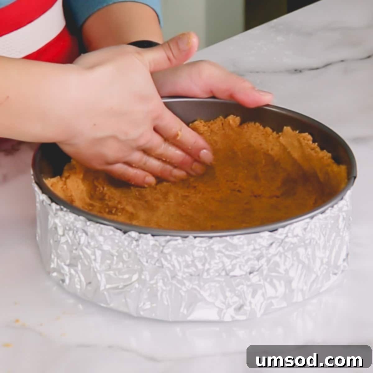 An image demonstrating the process of pressing the graham cracker crust evenly into a springform pan, extending up the sides.