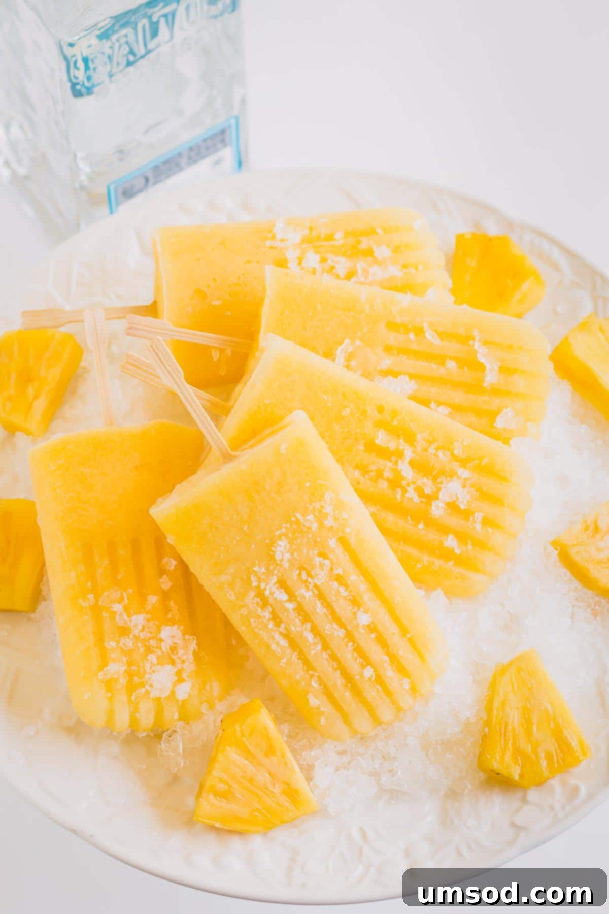 Close-up of a single boozy pineapple popsicle with visible pineapple chunks, glistening and frosted, on a bed of crushed ice.
