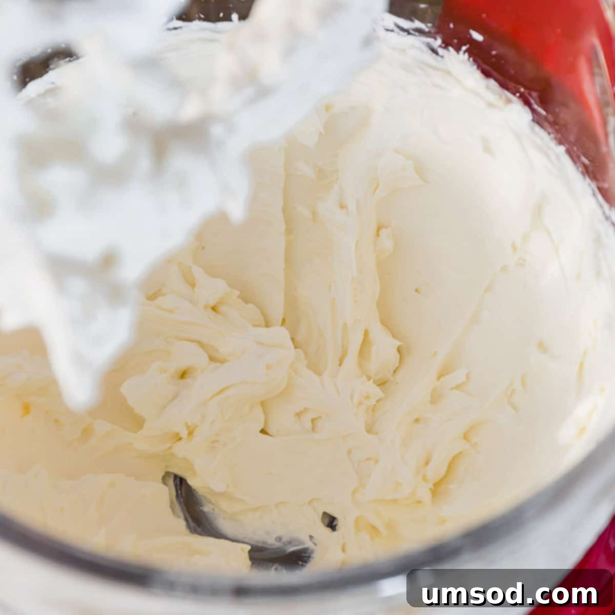 Smooth, whipped cream cheese filling in a clear glass bowl, attached to a stand mixer with a whisk attachment, ready for macaron assembly.