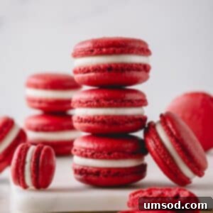 Three red velvet macarons stacked on top of each other and surrounded with more macarons, showcasing their perfect form.