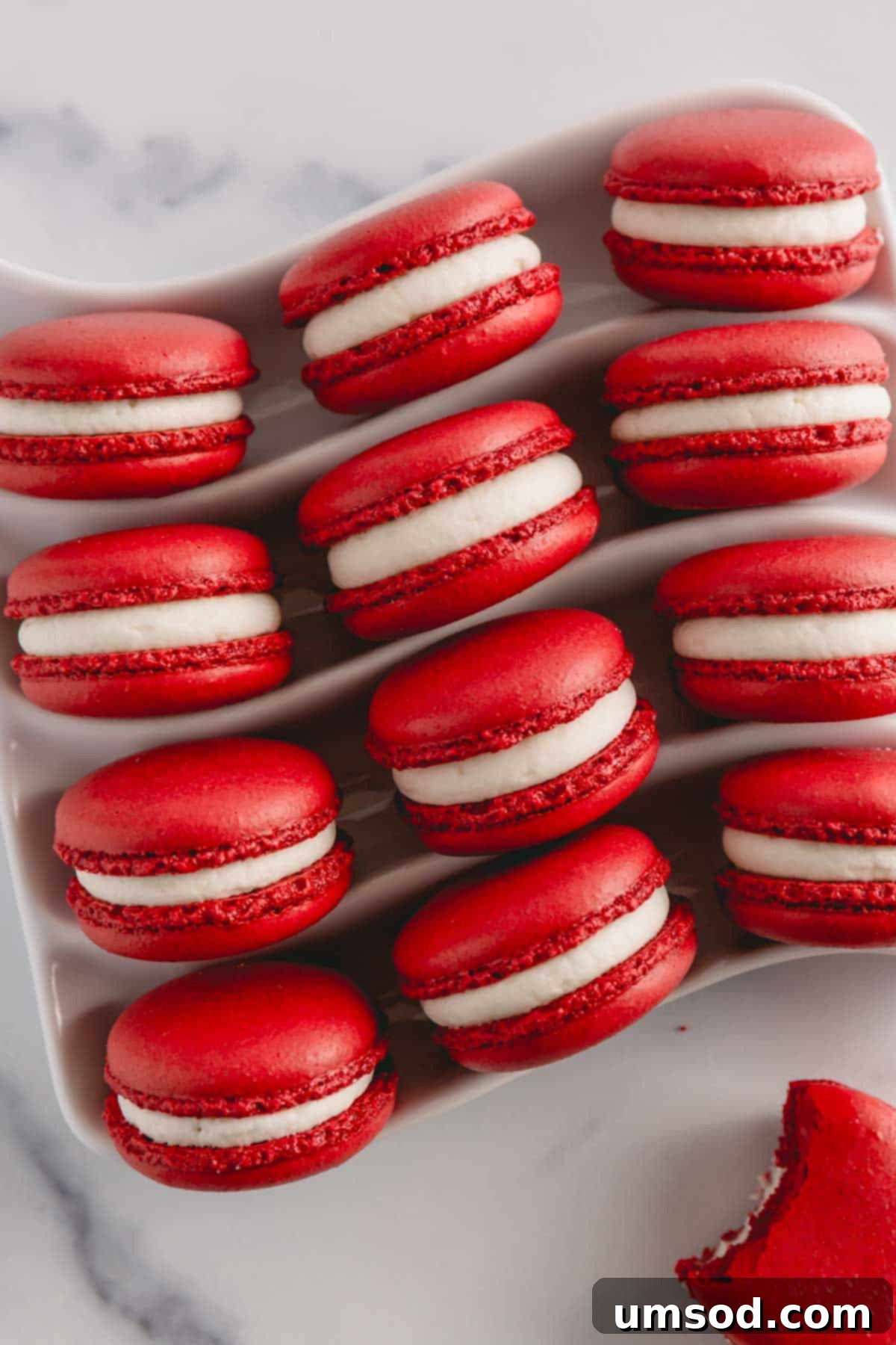 Vibrant red velvet macarons generously filled with smooth, white cream cheese frosting, elegantly arranged on a white serving platter.
