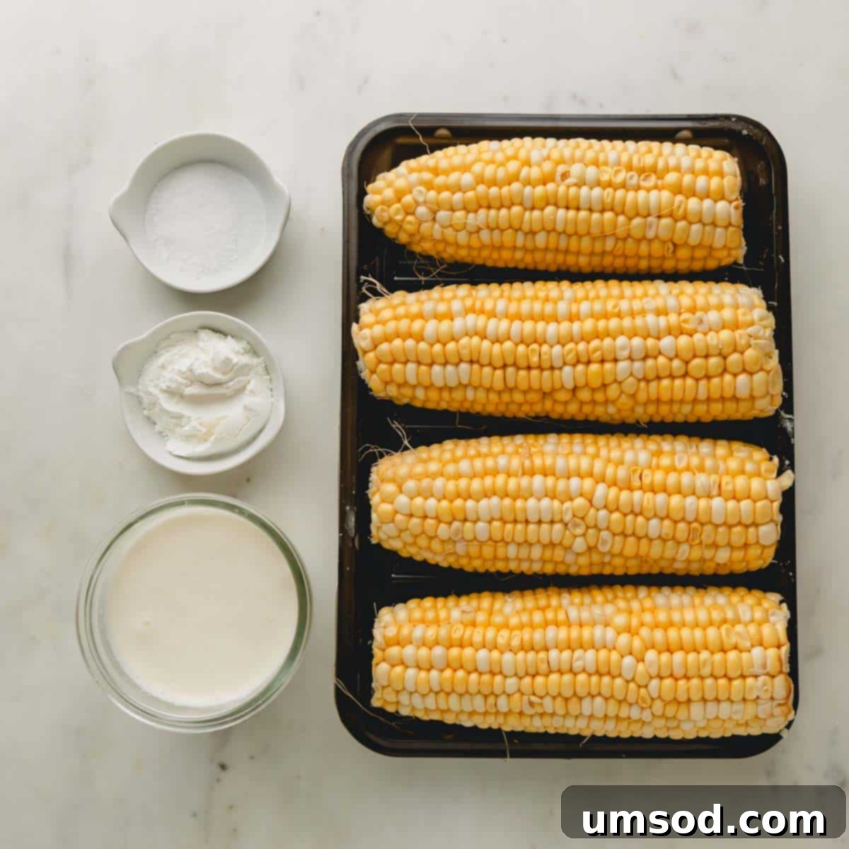Fresh ingredients for making homemade creamed corn laid out on a surface: corn, heavy cream, and cornstarch.