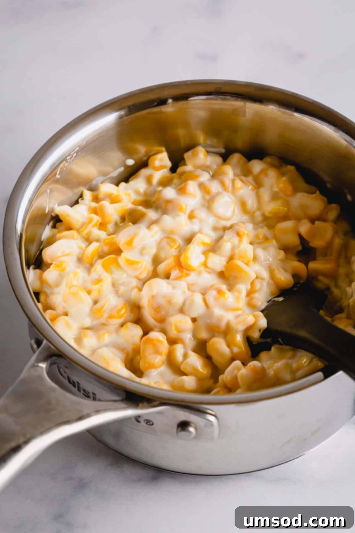 Creamed corn simmering in a saucepan on the stove, showing its creamy texture.