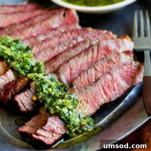 Flawless Ribeye: Grill Perfection with Zesty Chimichurri 5 Sliced grilled ribeye steak topped generously with fresh chimichurri sauce, ready to serve.