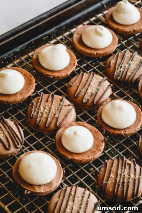 Chocolate macaron shell on a wire rack with a freshly piped dollop of marshmallow filling.
