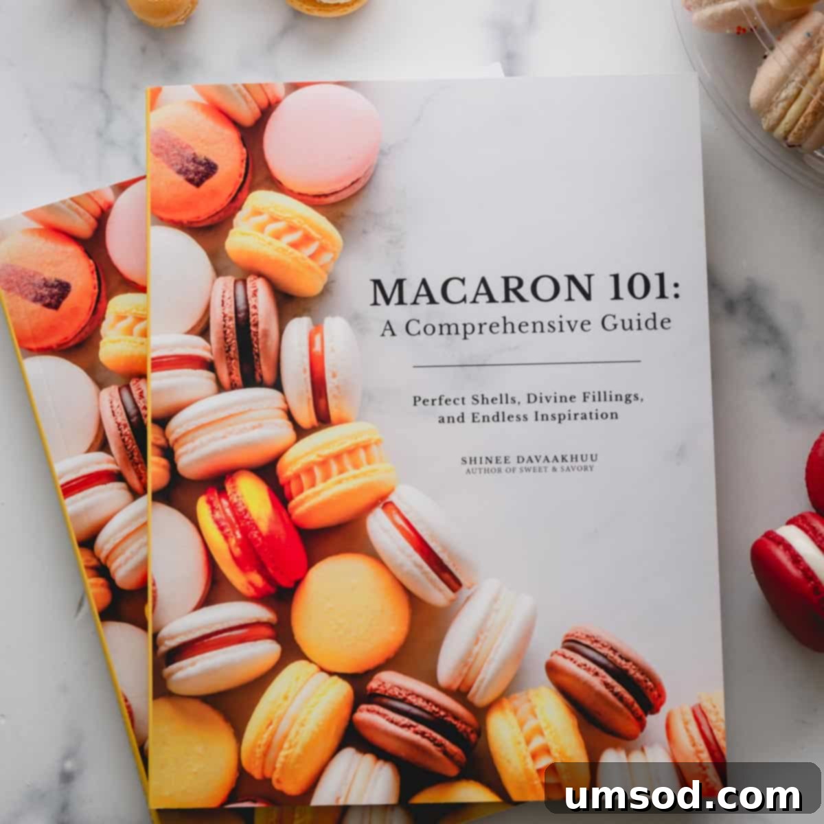 "Macaron 101" cookbook on a marble background, a comprehensive guide to macaron baking.