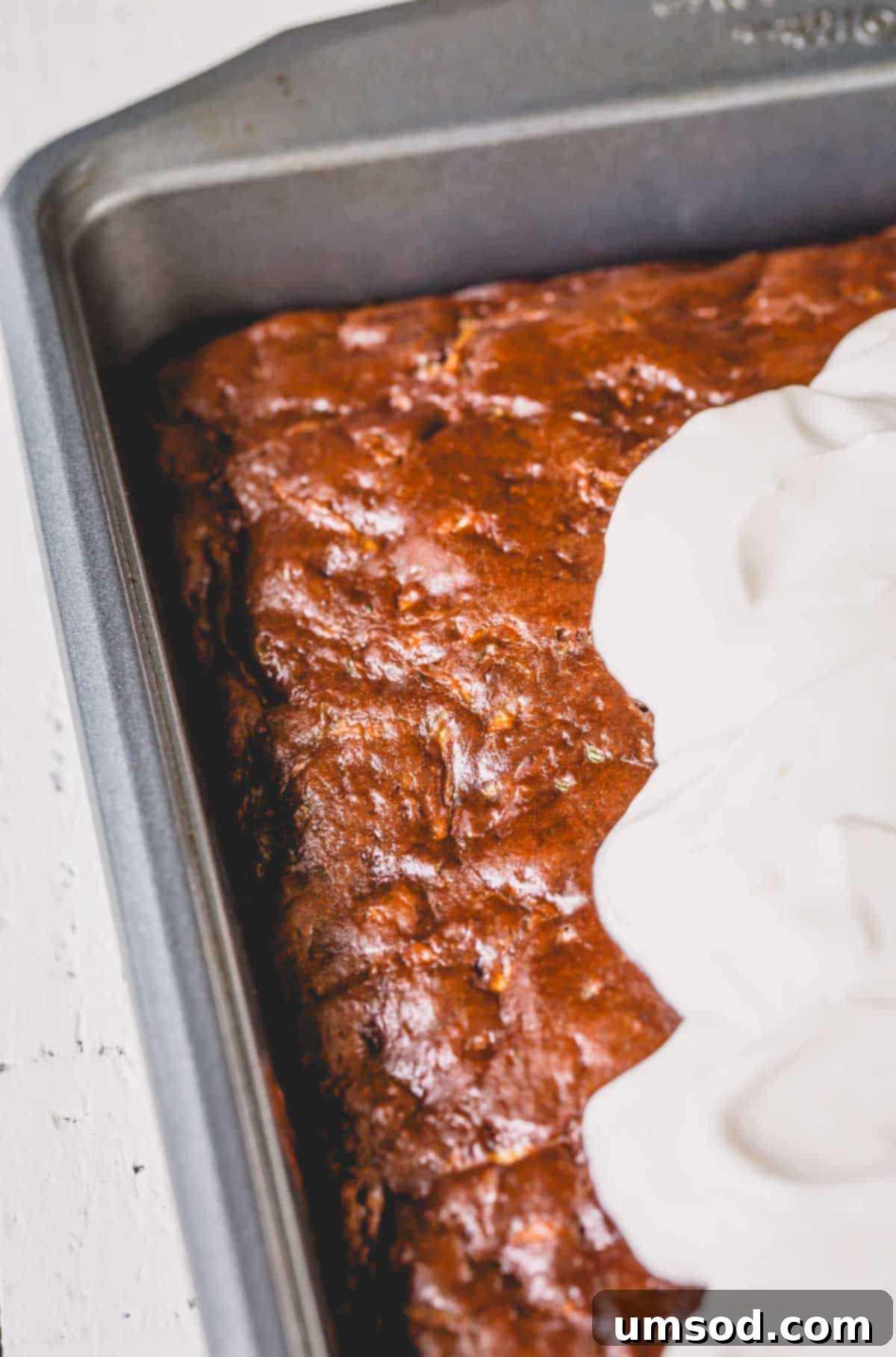 Fudgy Chocolate Zucchini Sheet Cake 3 Chocolate zucchini cake baking in a pan, topped with dollops of creamy sour cream frosting.